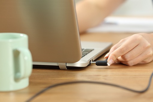 Imagem de um usuário verificando as conexões do cabo de alimentação em um notebook